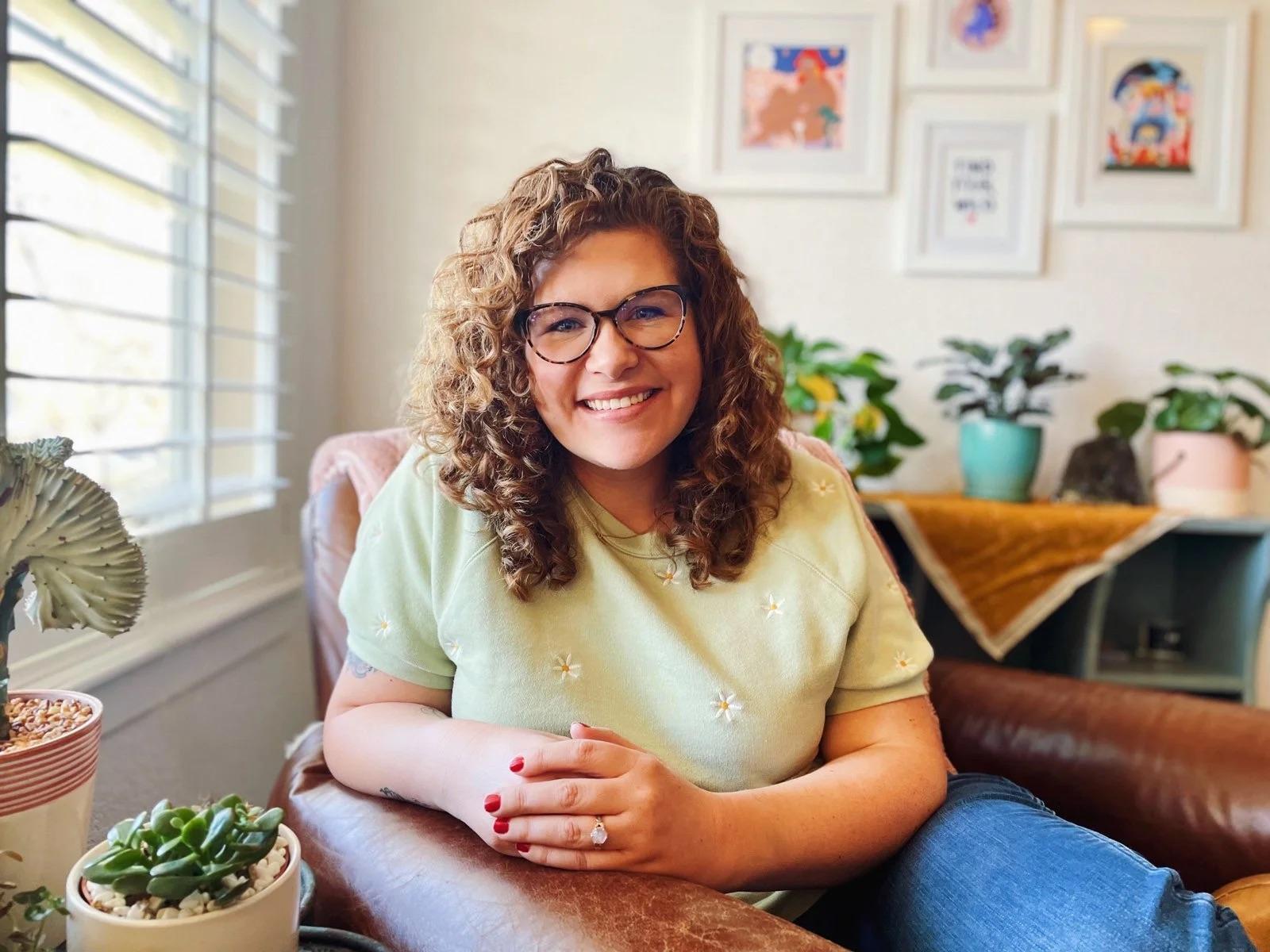 Portrait of Abby Howard smiling in a plant-filled reading nook
